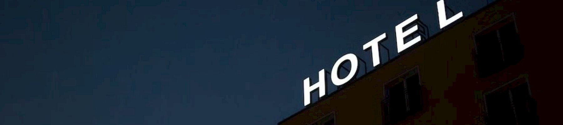 A building at night with a bright "HOTEL" sign; the letter "L" is unlit against a dark sky.