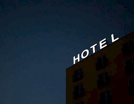 A building at night with a bright "HOTEL" sign; the letter "L" is unlit against a dark sky.